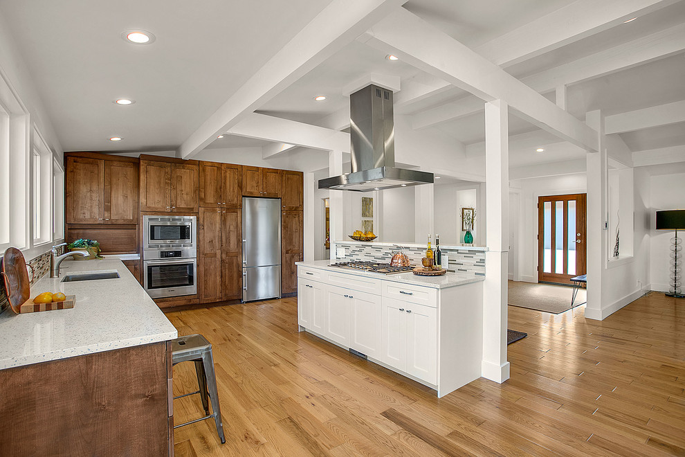 Photo of a medium sized midcentury l-shaped open plan kitchen in Los Angeles with a submerged sink, shaker cabinets, dark wood cabinets, engineered stone countertops, grey splashback, matchstick tiled splashback, stainless steel appliances, medium hardwood flooring, an island and brown floors.
