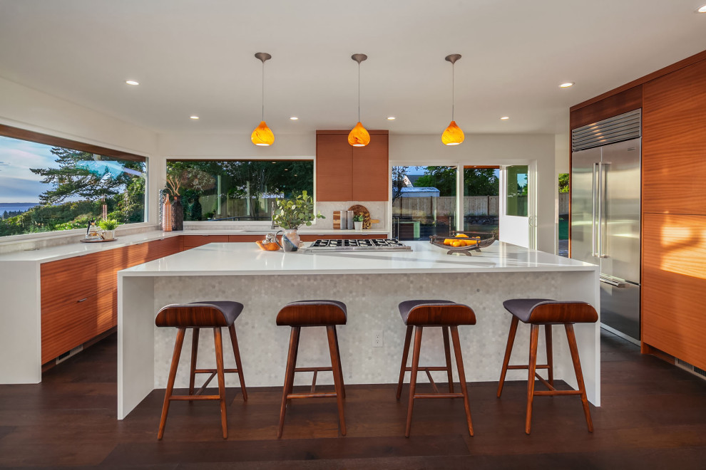 Inspiration for an expansive retro u-shaped open plan kitchen in Seattle with flat-panel cabinets, medium wood cabinets, engineered stone countertops, stainless steel appliances, dark hardwood flooring, an island, brown floors, white worktops, a submerged sink and window splashback.