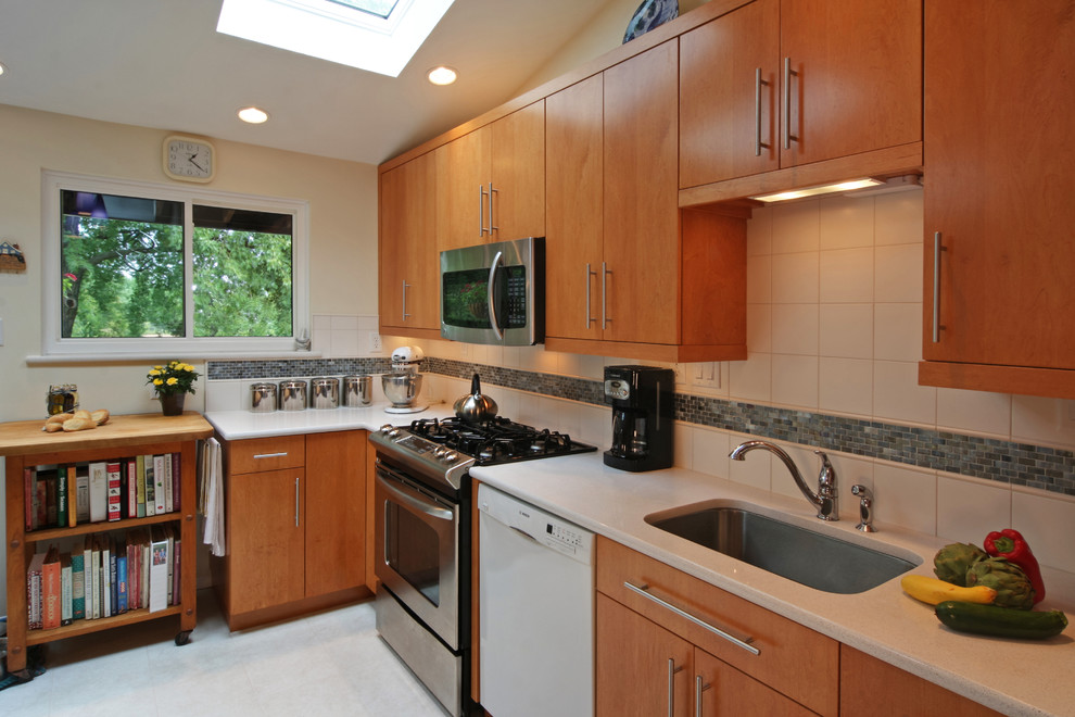 Bild på ett mellanstort funkis linjärt kök och matrum, med en undermonterad diskho, släta luckor, skåp i mellenmörkt trä, rostfria vitvaror, granitbänkskiva, vitt stänkskydd, stänkskydd i keramik och linoleumgolv