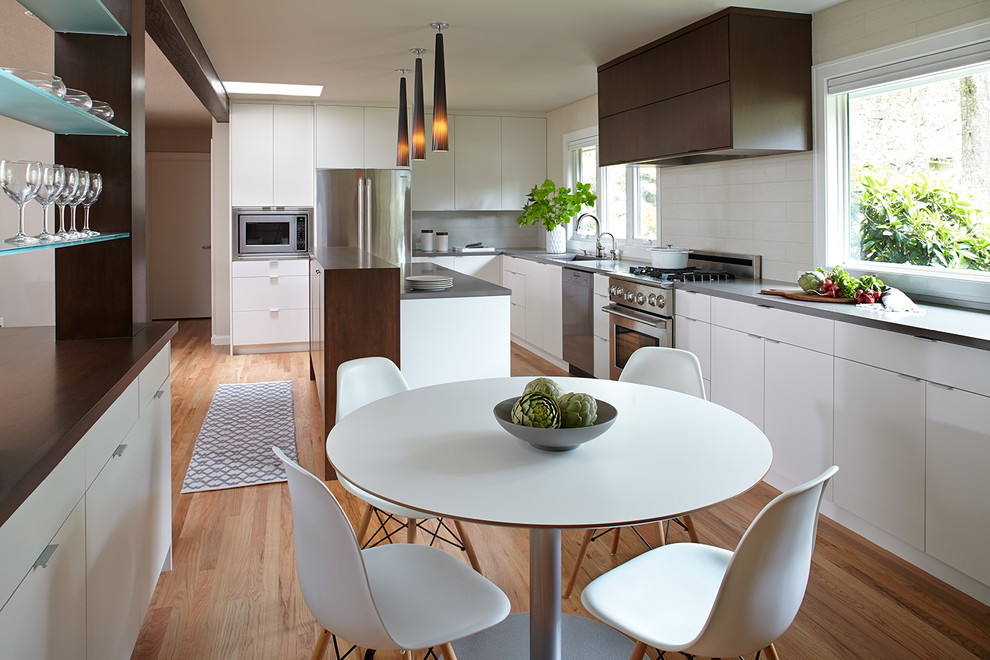 Example of a large trendy l-shaped medium tone wood floor eat-in kitchen design in Portland with an undermount sink, flat-panel cabinets, white cabinets, quartzite countertops, white backsplash, porcelain backsplash, stainless steel appliances and an island