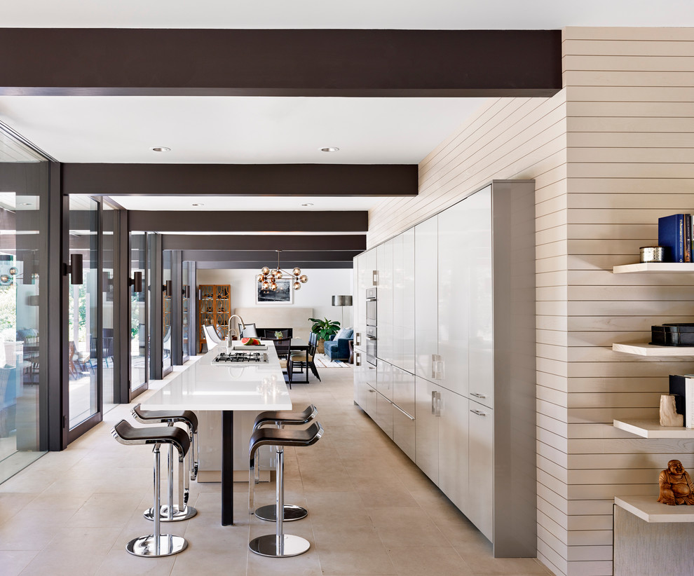 Photo of a large contemporary galley open plan kitchen in Austin with a submerged sink, flat-panel cabinets, white cabinets, composite countertops, white splashback, stainless steel appliances, ceramic flooring and an island.