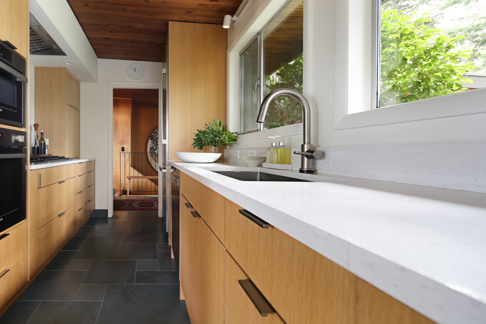 Idee per una cucina parallela minimalista di medie dimensioni con lavello sottopiano, ante lisce, ante in legno chiaro, top in quarzo composito, paraspruzzi bianco, elettrodomestici in acciaio inossidabile, pavimento in ardesia, pavimento grigio e top bianco
