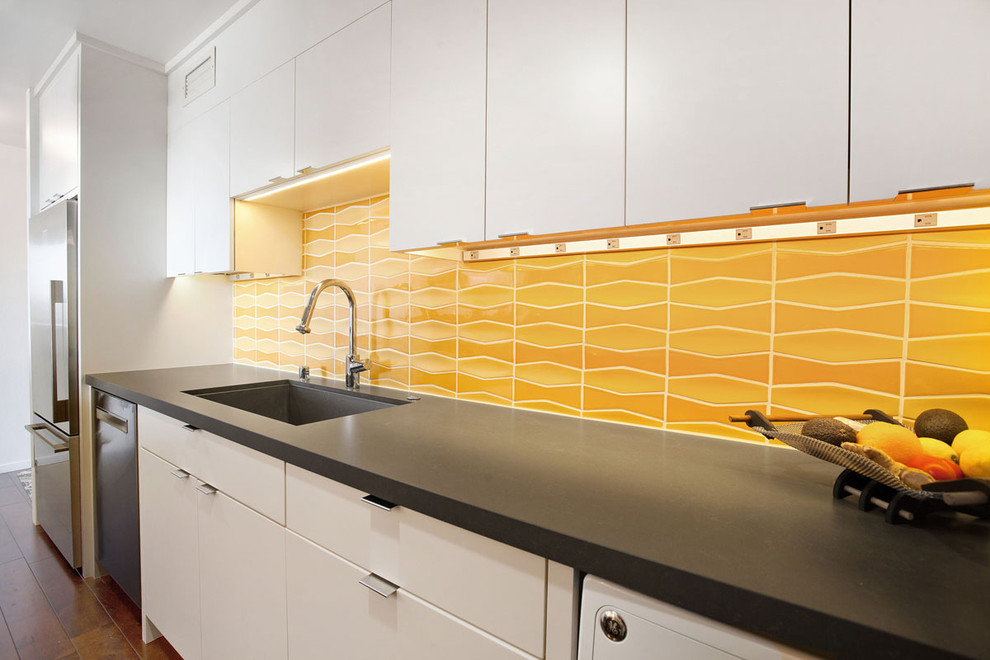 Inspiration for a small modern galley medium tone wood floor and brown floor enclosed kitchen remodel in San Francisco with a drop-in sink, flat-panel cabinets, white cabinets, quartz countertops, stainless steel appliances, ceramic backsplash and orange backsplash