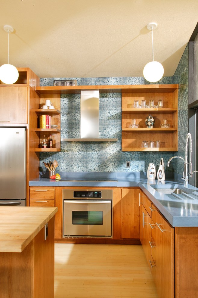 サクラメントにあるミッドセンチュリースタイルのおしゃれなキッチン (コンクリートカウンター、フラットパネル扉のキャビネット、中間色木目調キャビネット、青いキッチンパネル、モザイクタイルのキッチンパネル、シルバーの調理設備、青いキッチンカウンター) の写真