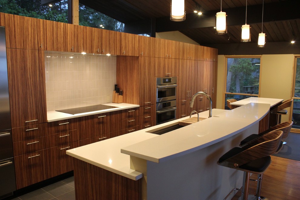 Large contemporary single-wall kitchen/diner in Seattle with flat-panel cabinets, medium wood cabinets, engineered stone countertops, white splashback, ceramic splashback, stainless steel appliances, ceramic flooring, an island and a submerged sink.
