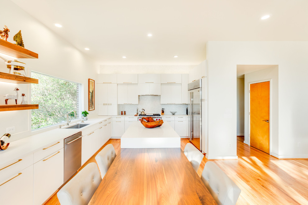 Example of a large minimalist u-shaped medium tone wood floor eat-in kitchen design in Birmingham with an undermount sink, flat-panel cabinets, white cabinets, quartz countertops, white backsplash, porcelain backsplash, stainless steel appliances, an island and white countertops
