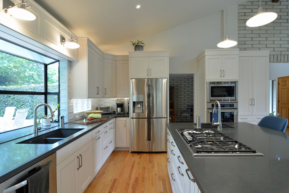 Inredning av ett modernt stort grå grått kök, med en undermonterad diskho, luckor med infälld panel, vita skåp, bänkskiva i kvarts, vitt stänkskydd, stänkskydd i porslinskakel, rostfria vitvaror, ljust trägolv, en köksö och beiget golv