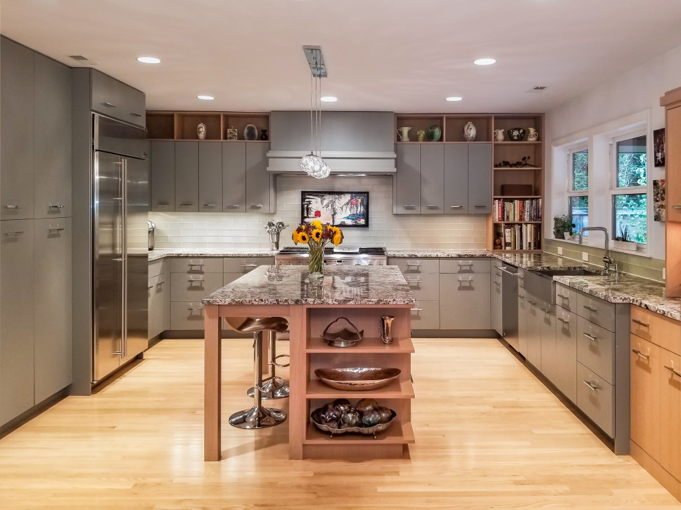 Bild på ett stort funkis grå grått kök, med en rustik diskho, släta luckor, grå skåp, granitbänkskiva, grått stänkskydd, stänkskydd i glaskakel, en köksö, beiget golv, rostfria vitvaror och ljust trägolv