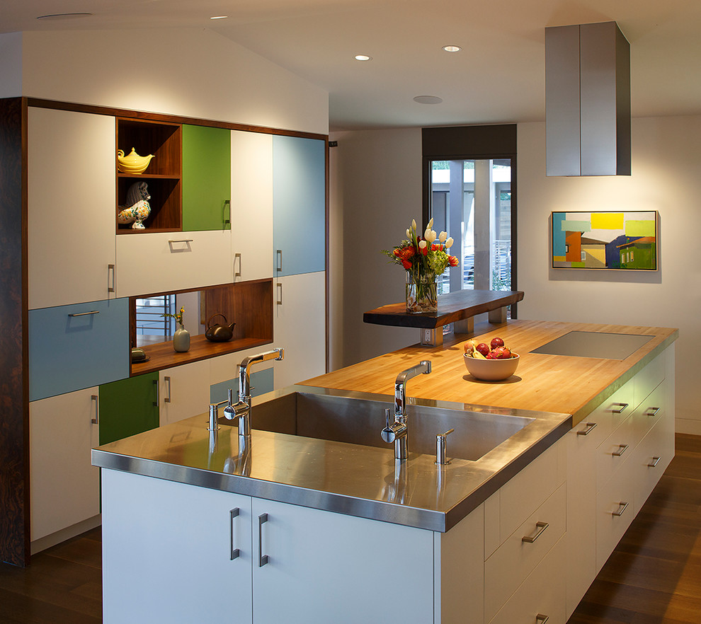 Eat-in kitchen - large 1960s galley medium tone wood floor eat-in kitchen idea in San Francisco with an integrated sink, flat-panel cabinets, white cabinets, wood countertops, white backsplash, glass sheet backsplash, stainless steel appliances and an island