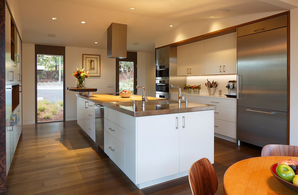 Inspiration for a large mid-century modern galley medium tone wood floor eat-in kitchen remodel in San Francisco with flat-panel cabinets, white cabinets, wood countertops, stainless steel appliances, an island, white backsplash, glass sheet backsplash and an integrated sink
