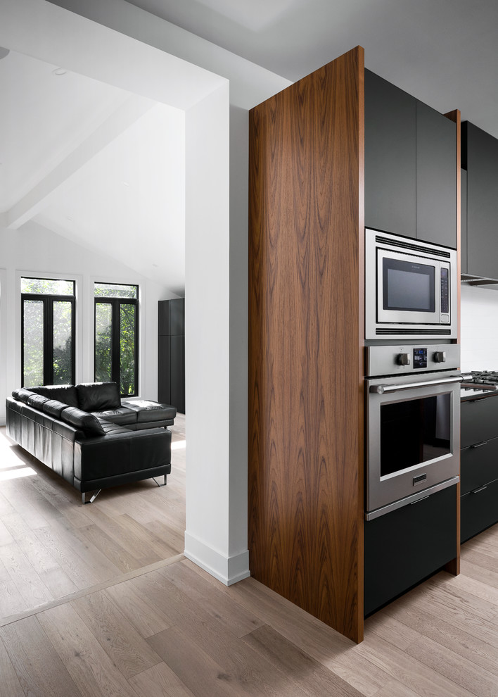 Bild på ett mellanstort retro svart svart kök, med en undermonterad diskho, släta luckor, svarta skåp, bänkskiva i kvarts, vitt stänkskydd, stänkskydd i tunnelbanekakel, rostfria vitvaror, ljust trägolv, en köksö och brunt golv