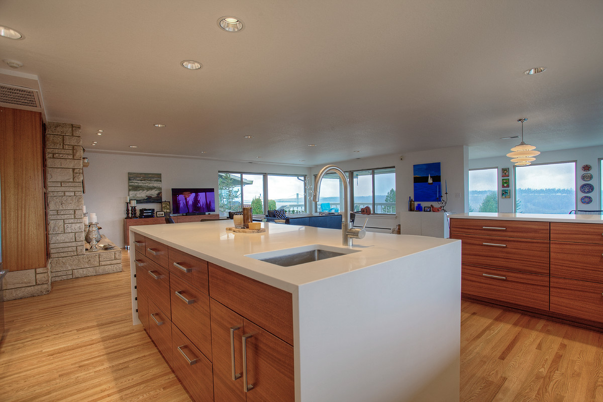 This is an example of a large retro u-shaped open plan kitchen in Seattle with a submerged sink, flat-panel cabinets, medium wood cabinets, engineered stone countertops, white splashback, metro tiled splashback, stainless steel appliances, light hardwood flooring and an island.