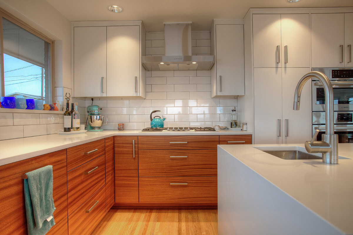 Design ideas for a large retro u-shaped open plan kitchen in Seattle with a submerged sink, flat-panel cabinets, medium wood cabinets, engineered stone countertops, white splashback, metro tiled splashback, stainless steel appliances, light hardwood flooring and an island.
