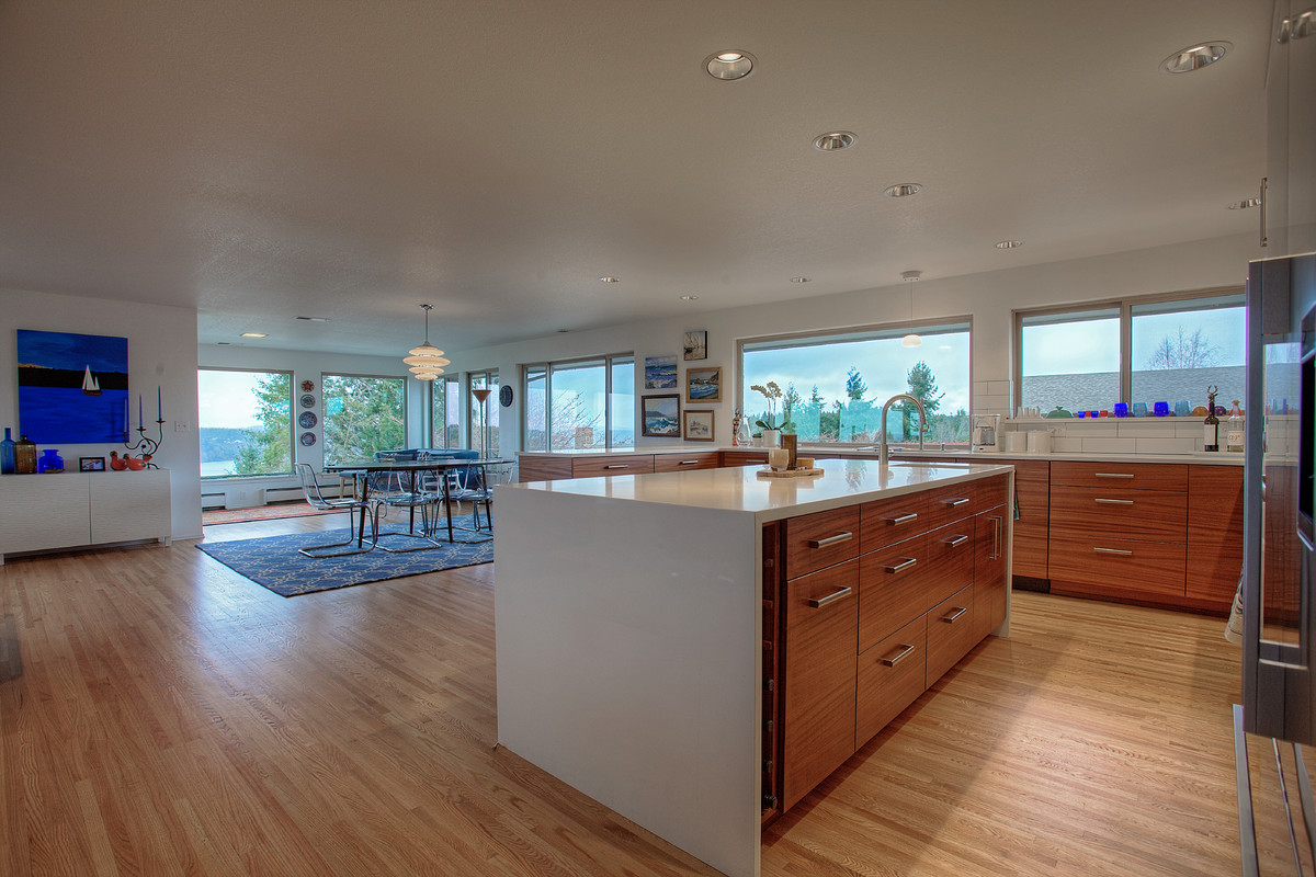 Photo of a large midcentury u-shaped open plan kitchen in Seattle with a submerged sink, flat-panel cabinets, medium wood cabinets, engineered stone countertops, white splashback, metro tiled splashback, stainless steel appliances, light hardwood flooring and an island.
