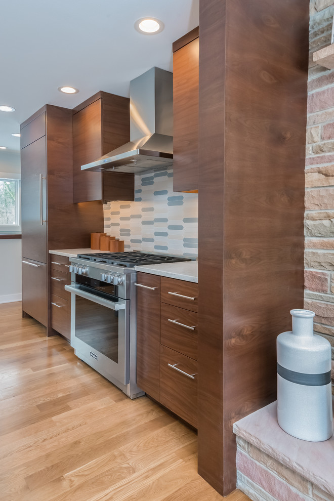 Example of a mid-sized 1950s galley light wood floor and beige floor open concept kitchen design in New York with an undermount sink, flat-panel cabinets, dark wood cabinets, quartz countertops, multicolored backsplash, ceramic backsplash, paneled appliances, an island and white countertops