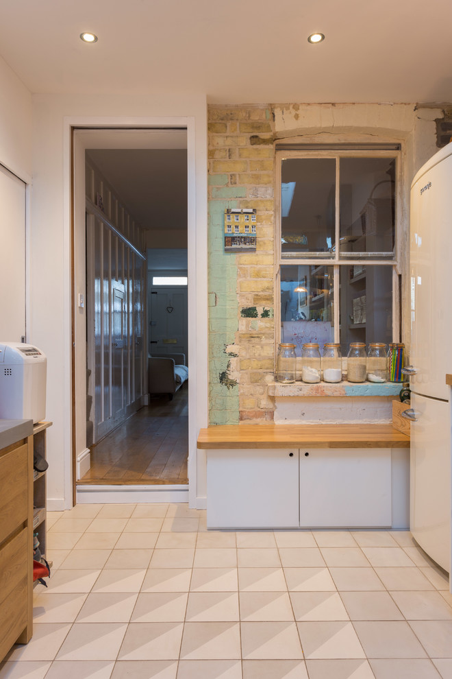 Inspiration for a small shabby-chic style l-shaped ceramic tile and multicolored floor open concept kitchen remodel in Cambridgeshire with a farmhouse sink, flat-panel cabinets, white cabinets, wood countertops, white backsplash, ceramic backsplash and stainless steel appliances