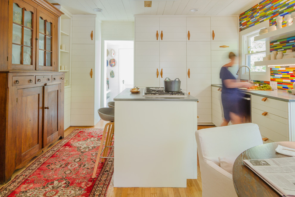 Photo of a medium sized midcentury kitchen/diner in Austin with white cabinets, concrete worktops, multi-coloured splashback, glass tiled splashback, light hardwood flooring and an island.