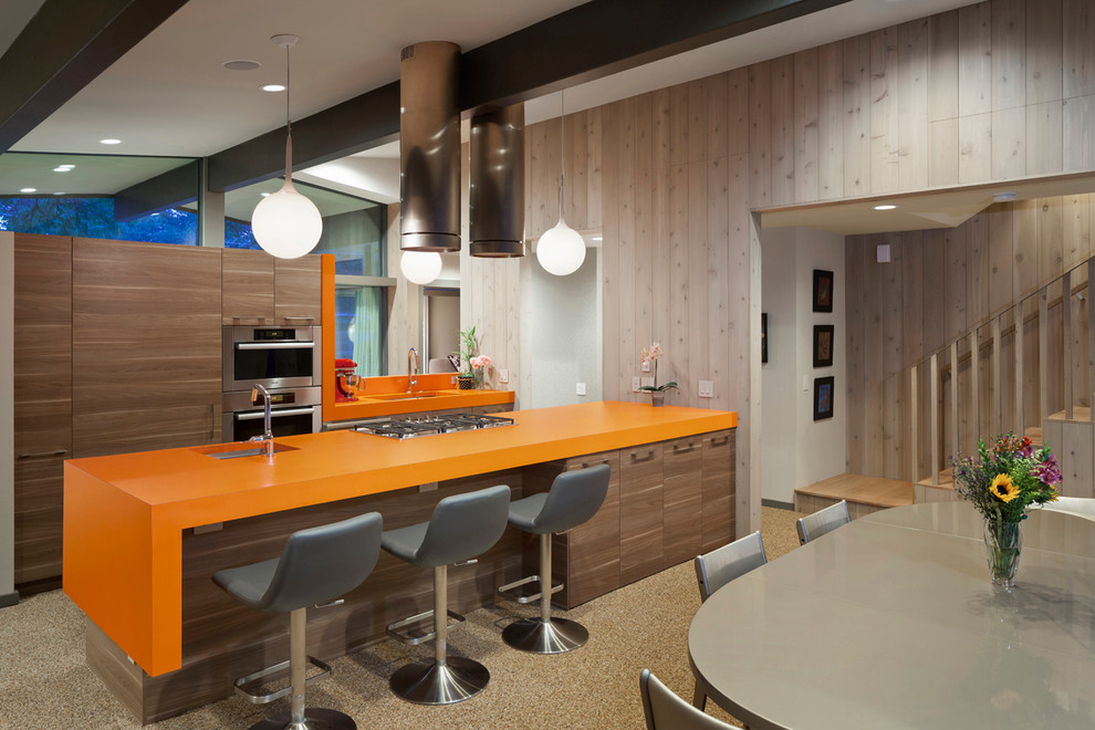 Zweizeilige Retro Wohnküche mit flächenbündigen Schrankfronten, dunklen Holzschränken, Küchengeräten aus Edelstahl, Kücheninsel und oranger Arbeitsplatte in Austin