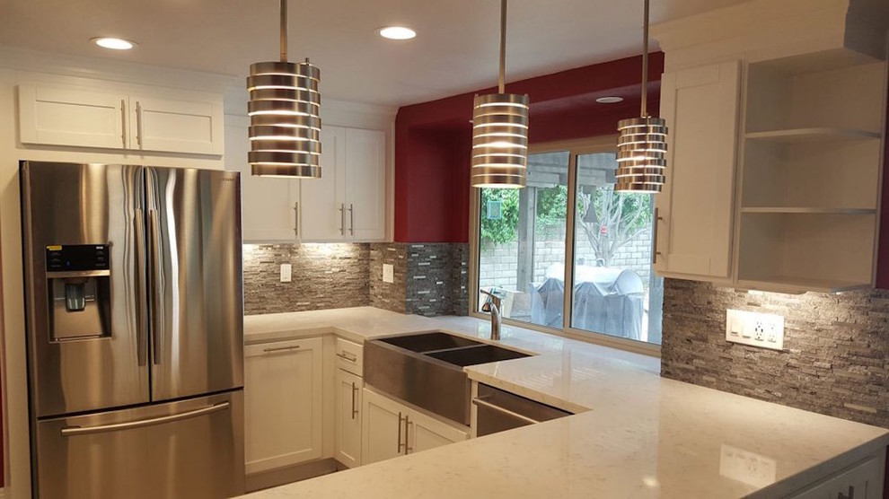 Photo of a medium sized retro u-shaped open plan kitchen in Los Angeles with a belfast sink, shaker cabinets, white cabinets, engineered stone countertops, grey splashback, stone tiled splashback, stainless steel appliances, a breakfast bar, light hardwood flooring and beige floors.
