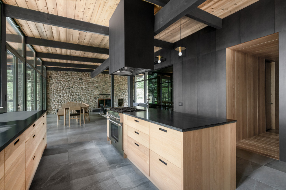 Zweizeilige Mid-Century Küche mit flächenbündigen Schrankfronten, hellen Holzschränken, Kücheninsel, grauem Boden, schwarzer Arbeitsplatte und Holzdecke in Montreal