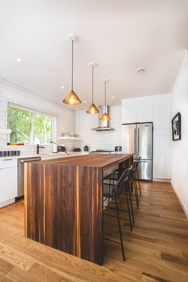 Esempio di un cucina con isola centrale minimal con ante lisce, ante bianche, elettrodomestici in acciaio inossidabile e pavimento in legno massello medio
