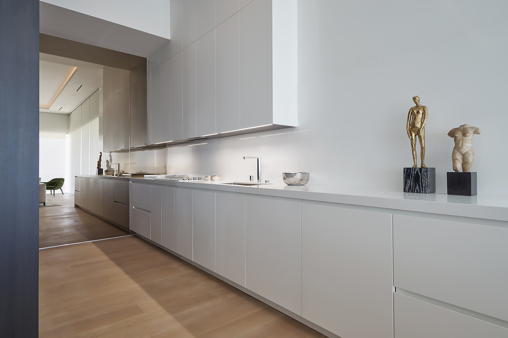 Large modern galley kitchen/diner in Los Angeles with a submerged sink, flat-panel cabinets, white cabinets, white splashback, light hardwood flooring and beige floors.