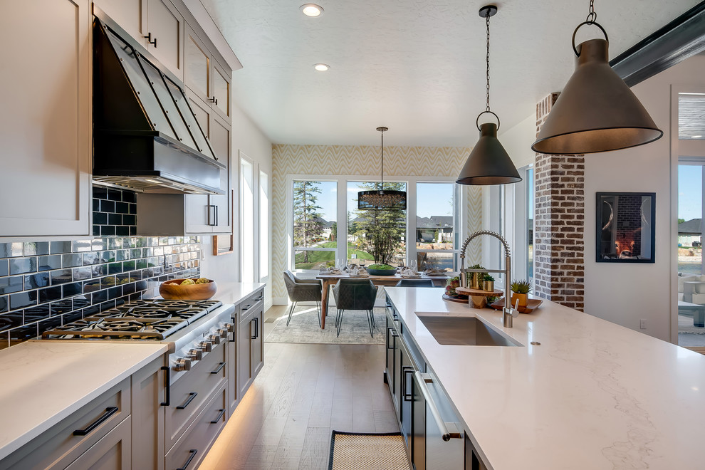 Inspiration for a large transitional u-shaped medium tone wood floor and brown floor eat-in kitchen remodel in Boise with an undermount sink, shaker cabinets, gray cabinets, quartz countertops, black backsplash, subway tile backsplash, stainless steel appliances, an island and white countertops