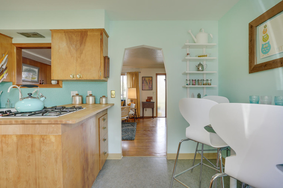 Bild på ett mellanstort 60 tals kök, med en nedsänkt diskho, släta luckor, skåp i ljust trä, laminatbänkskiva, blått stänkskydd, vita vitvaror, linoleumgolv, en halv köksö och turkost golv