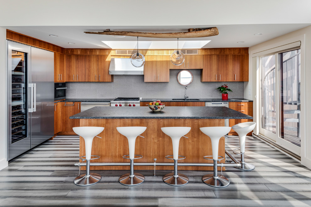 Large coastal l-shaped kitchen in Boston with a submerged sink, flat-panel cabinets, medium wood cabinets, grey splashback, stainless steel appliances, an island and grey floors.
