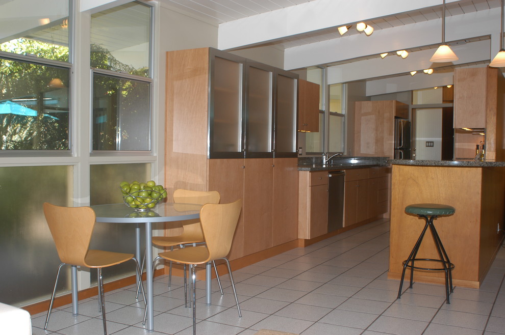 Exempel på ett litet 50 tals kök, med en undermonterad diskho, släta luckor, skåp i ljust trä, granitbänkskiva, flerfärgad stänkskydd, rostfria vitvaror, klinkergolv i porslin och en halv köksö