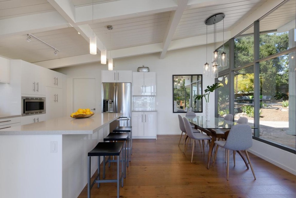 Zweizeilige Retro Wohnküche mit flächenbündigen Schrankfronten, weißen Schränken, Küchengeräten aus Edelstahl, braunem Holzboden, Kücheninsel, braunem Boden und grauer Arbeitsplatte in Santa Barbara