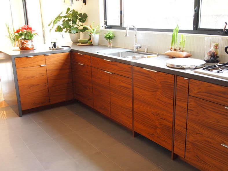 This is an example of a medium sized midcentury galley kitchen in Santa Barbara with flat-panel cabinets, medium wood cabinets, engineered stone countertops, white splashback, glass tiled splashback, stainless steel appliances, ceramic flooring, a breakfast bar and a submerged sink.