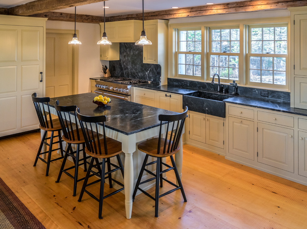 Foto på ett stort vintage linjärt kök och matrum, med en rustik diskho, luckor med upphöjd panel, vita skåp, bänkskiva i täljsten, svart stänkskydd, stänkskydd i sten, integrerade vitvaror, ljust trägolv och en köksö