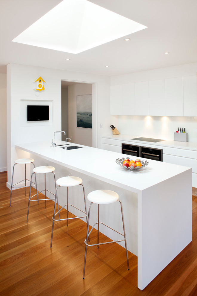 Cette image montre une cuisine minimaliste avec un placard à porte plane, des portes de placard blanches et une péninsule.