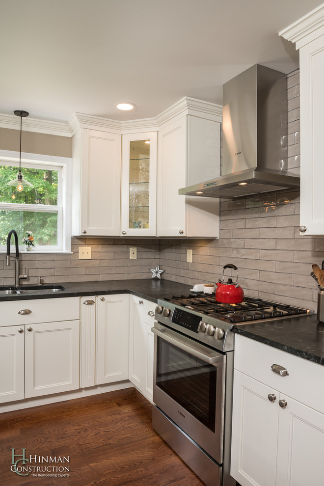 Example of a mid-sized arts and crafts l-shaped medium tone wood floor and brown floor open concept kitchen design in Other with an undermount sink, recessed-panel cabinets, white cabinets, granite countertops, gray backsplash, glass tile backsplash, stainless steel appliances, an island and black countertops