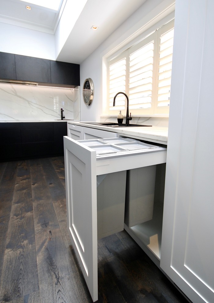 Exempel på ett mycket stort modernt vit vitt kök, med en nedsänkt diskho, luckor med upphöjd panel, svarta skåp, bänkskiva i kvarts, vitt stänkskydd, stänkskydd i sten, svarta vitvaror, mörkt trägolv, flera köksöar och svart golv