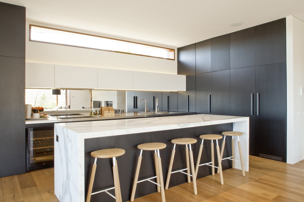 Cette photo montre une grande cuisine parallèle tendance en bois foncé avec un placard à porte plane, plan de travail en marbre, une crédence miroir, parquet clair et îlot.