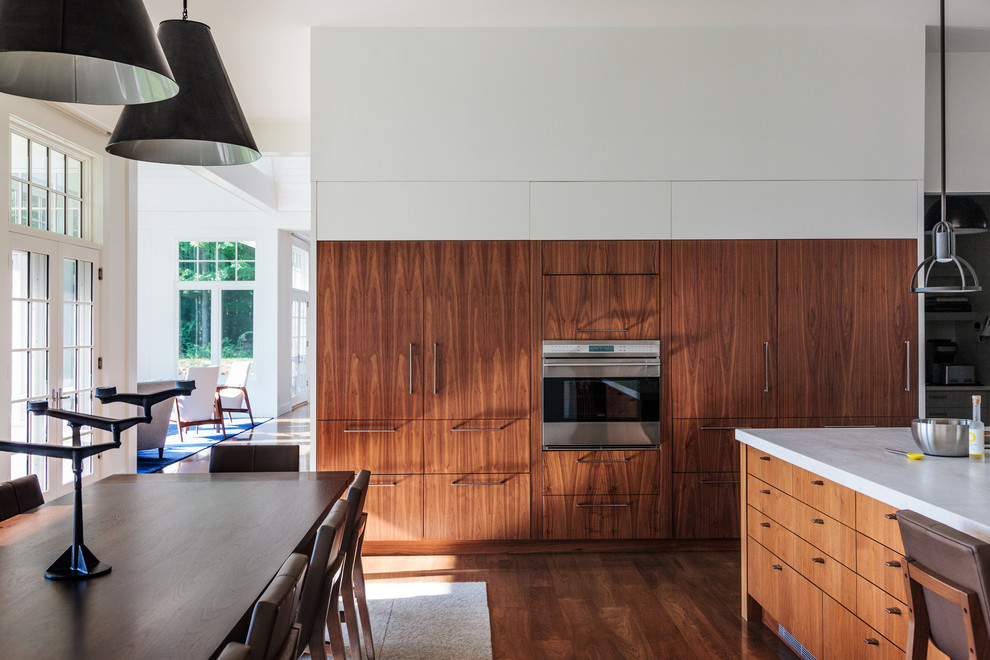 Ejemplo de cocina comedor tradicional renovada con armarios con paneles lisos, puertas de armario de madera en tonos medios, encimera de mármol, electrodomésticos de acero inoxidable, suelo de madera oscura y una isla