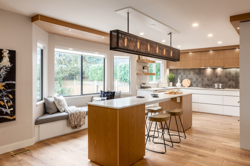 Moderne Küche mit Unterbauwaschbecken, flächenbündigen Schrankfronten, hellbraunen Holzschränken, Küchenrückwand in Grau, hellem Holzboden und Kücheninsel in Vancouver