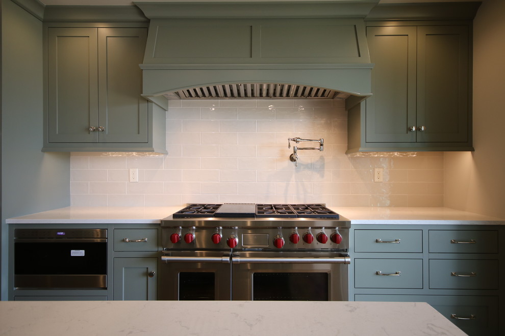Klassisk inredning av ett mellanstort kök, med en undermonterad diskho, öppna hyllor, gröna skåp, bänkskiva i kvarts, vitt stänkskydd, stänkskydd i glaskakel, rostfria vitvaror, mörkt trägolv och en köksö