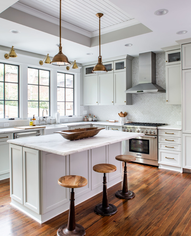 Inspiration for a traditional l-shaped kitchen in Atlanta with a belfast sink, recessed-panel cabinets, white cabinets, white splashback, stainless steel appliances, dark hardwood flooring, an island, brown floors and white worktops.