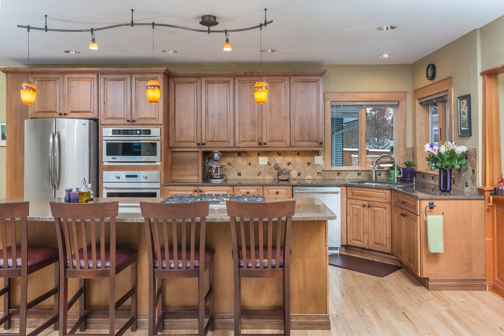 Mid-sized elegant l-shaped light wood floor open concept kitchen photo in Other with an undermount sink, raised-panel cabinets, medium tone wood cabinets, quartz countertops, brown backsplash, stone tile backsplash, stainless steel appliances and an island