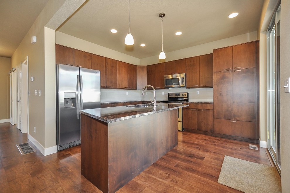 Large classic l-shaped open plan kitchen in Orange County with a submerged sink, flat-panel cabinets, dark wood cabinets, granite worktops, stainless steel appliances, laminate floors and an island.