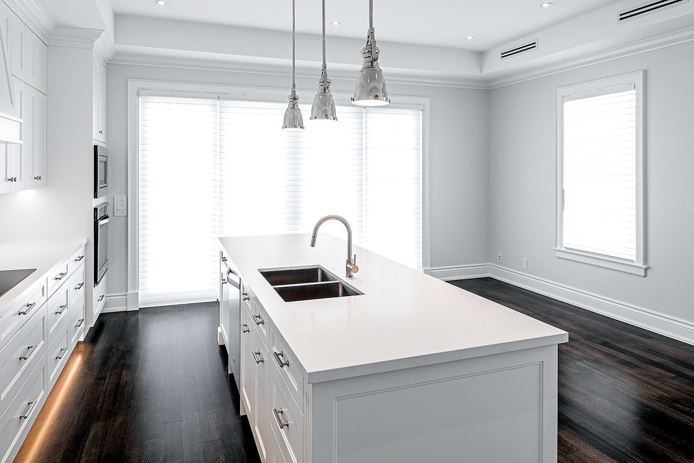 Exempel på ett mellanstort klassiskt linjärt kök och matrum, med en dubbel diskho, luckor med profilerade fronter, vita skåp, bänkskiva i kvarts, vitt stänkskydd, stänkskydd i sten, rostfria vitvaror, mellanmörkt trägolv och en köksö