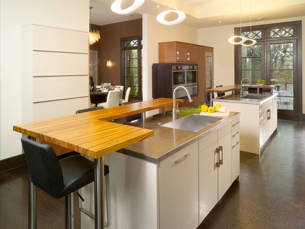 Example of a minimalist enclosed kitchen design in Atlanta with stainless steel countertops, an integrated sink, flat-panel cabinets, stainless steel appliances and beige cabinets