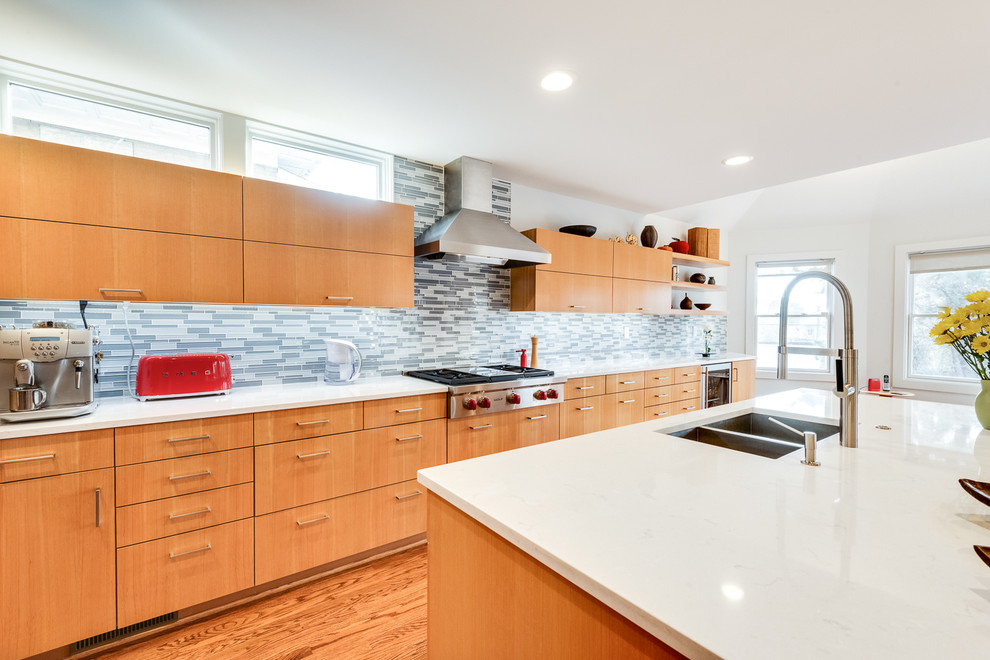 Modern inredning av ett mellanstort vit vitt kök, med en undermonterad diskho, släta luckor, skåp i ljust trä, bänkskiva i kvarts, grått stänkskydd, stänkskydd i glaskakel, rostfria vitvaror, mellanmörkt trägolv, en köksö och brunt golv