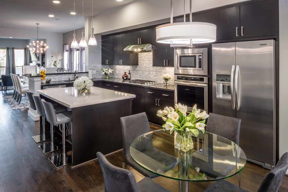 Large modern l-shaped kitchen/diner in Houston with a submerged sink, flat-panel cabinets, dark wood cabinets, engineered stone countertops, grey splashback, glass tiled splashback, stainless steel appliances, dark hardwood flooring and an island.