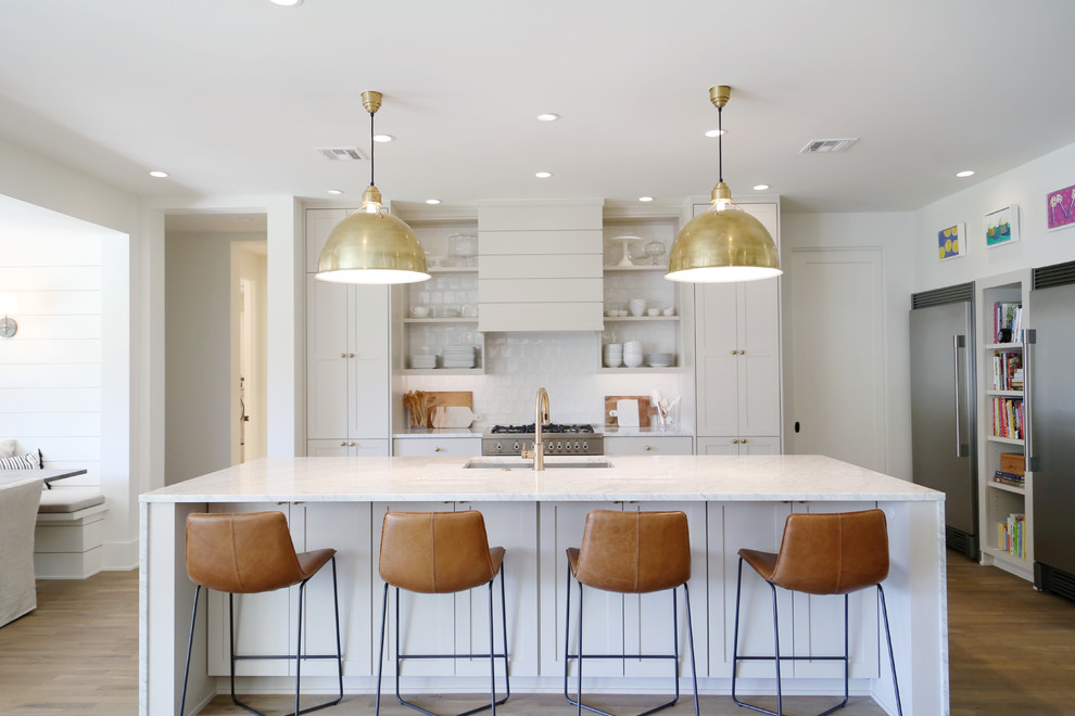 Large trendy l-shaped light wood floor open concept kitchen photo in Other with an undermount sink, shaker cabinets, white cabinets, marble countertops, white backsplash, subway tile backsplash, stainless steel appliances and an island