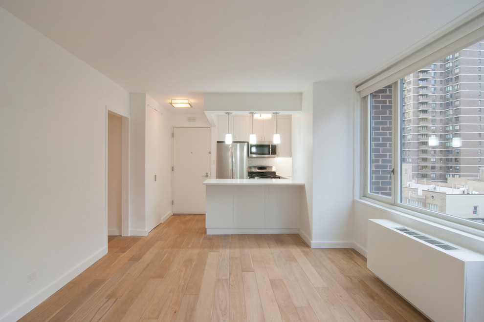 Example of a small minimalist u-shaped light wood floor and beige floor eat-in kitchen design in New York with an undermount sink, shaker cabinets, white cabinets, quartz countertops, white backsplash, glass tile backsplash, stainless steel appliances and a peninsula