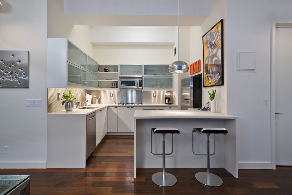 This is an example of a contemporary l-shaped kitchen in New York with flat-panel cabinets, white cabinets, metallic splashback and stainless steel appliances.